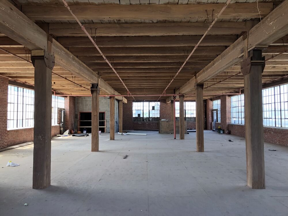 The bare factory floor before restoration, with original timber posts and steel sash windows