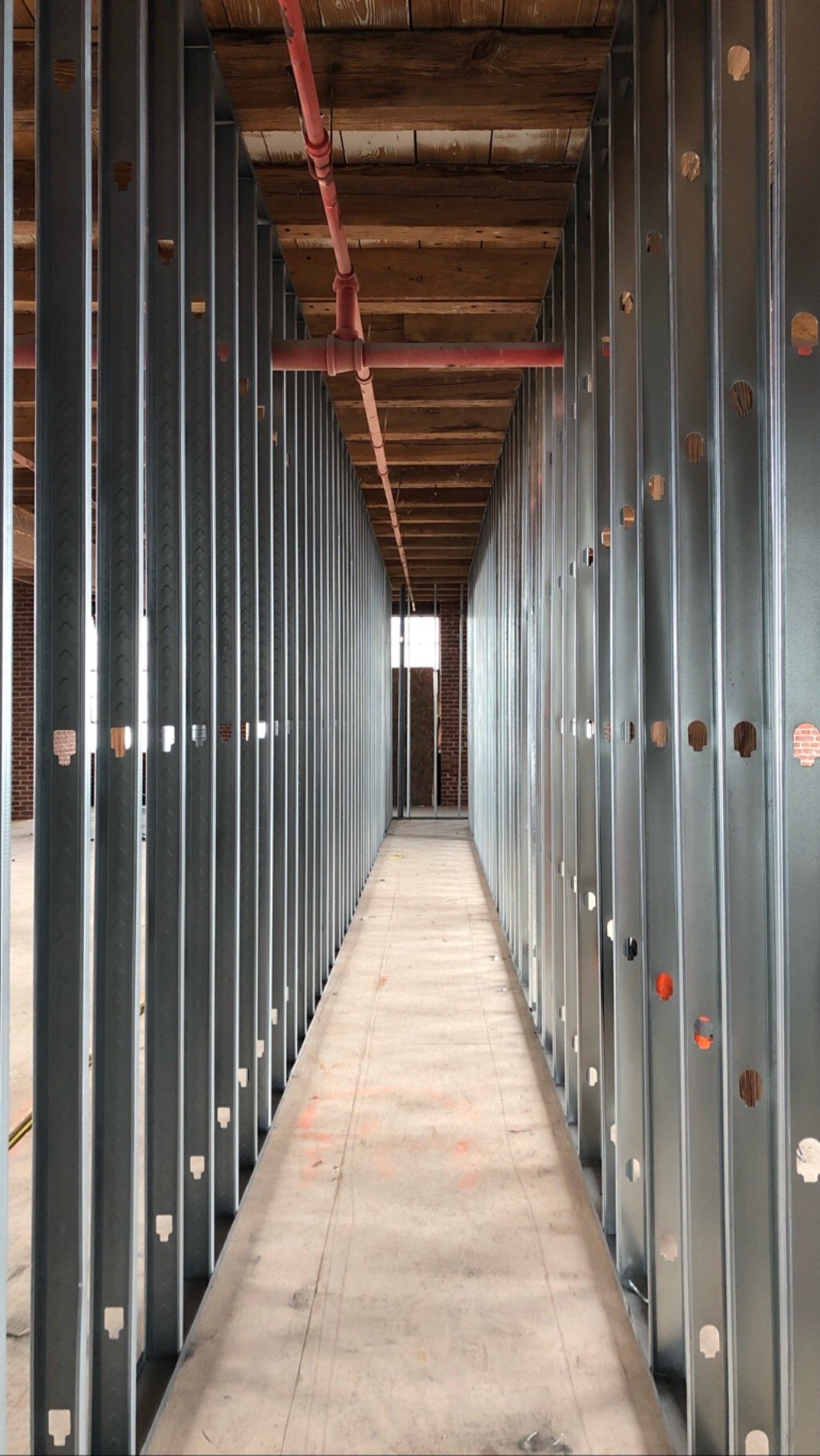 A corridor at Billy Penn Studios framed in metal studs, under the original wood joists and a red sprinkler main