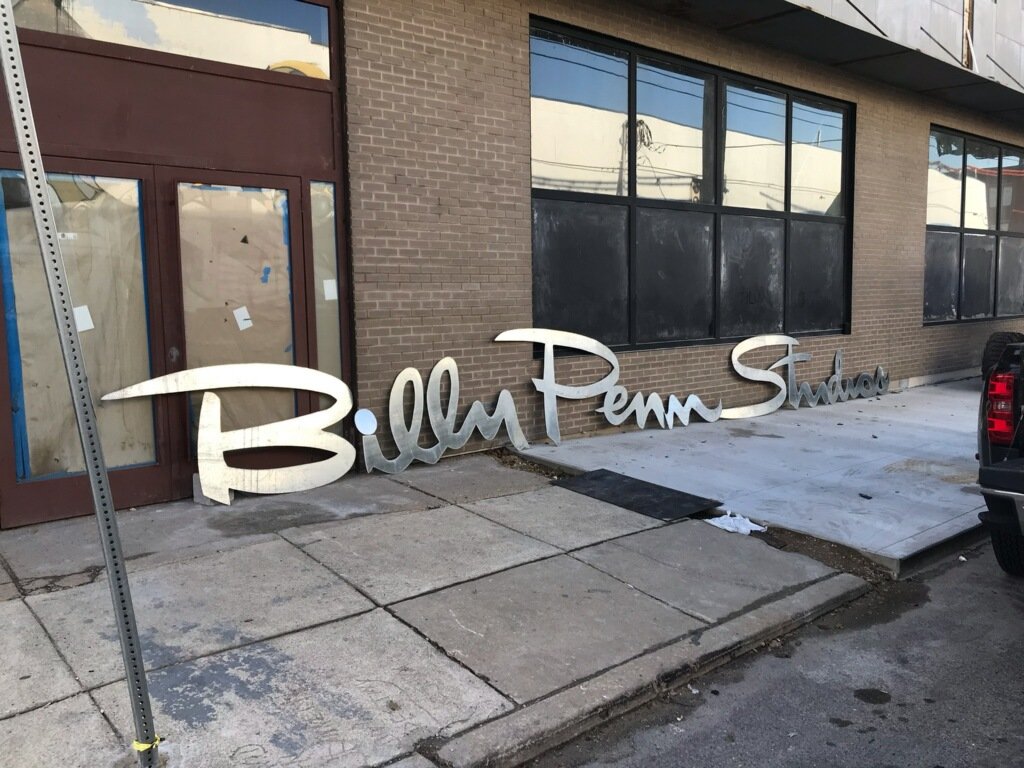 The on-site metal shop at Billy Penn Studios, with racked steel stock, welding gear and workbenches under red painted structural steel