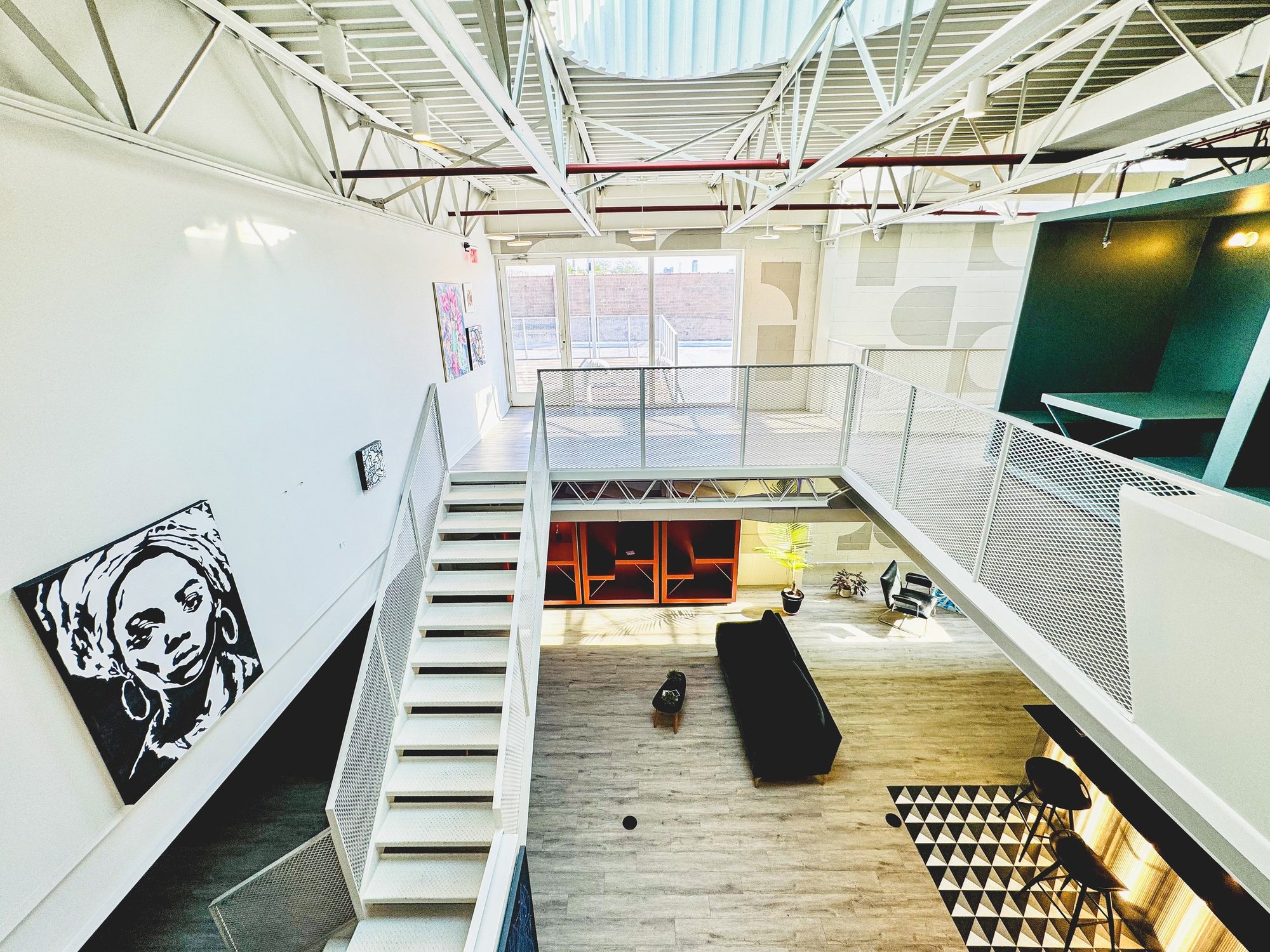 The atrium lounge at Billy Penn Studios coworking, with sofas, orange work booths and the stair to the mezzanine
