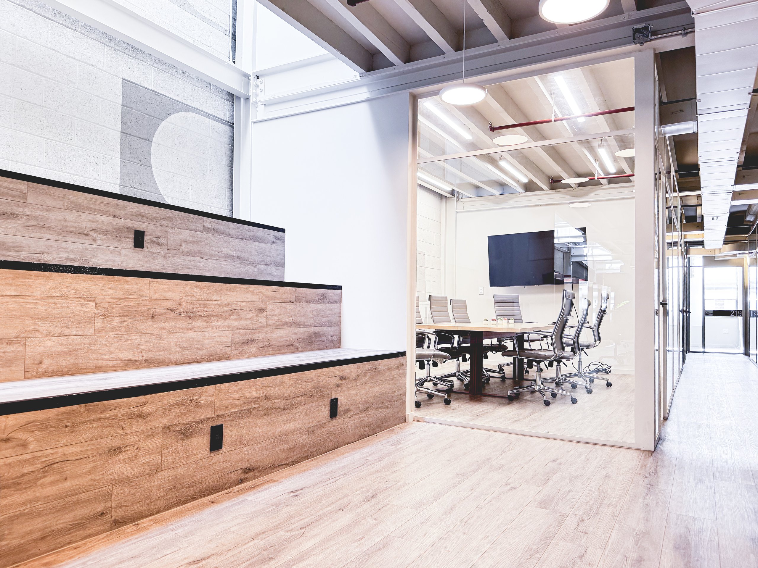 Tiered wood bleacher seating beside a glass walled conference room at Billy Penn Studios coworking