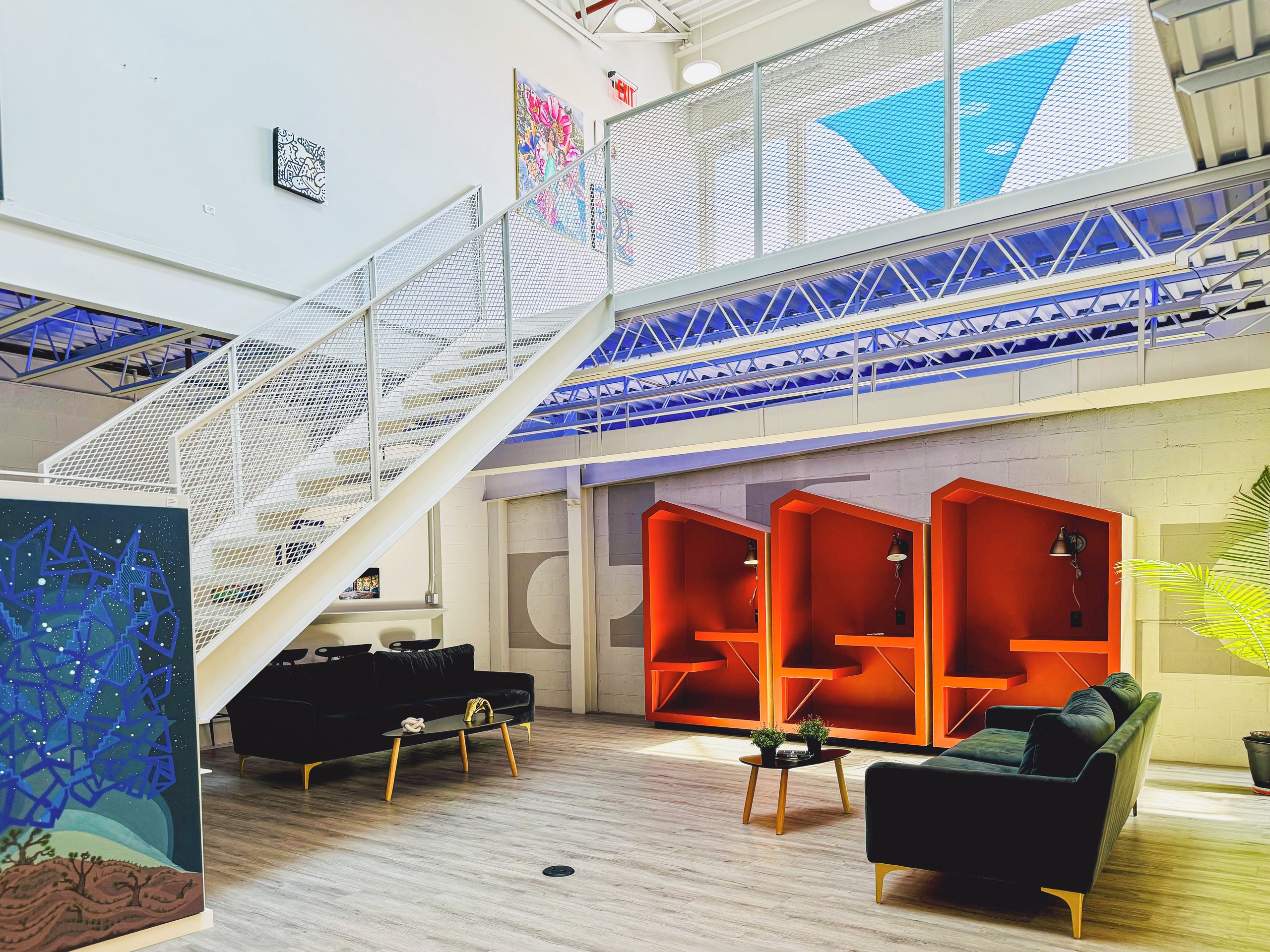 The double height coworking lounge at Billy Penn Studios, with sofas, work booths and the stair to the mezzanine