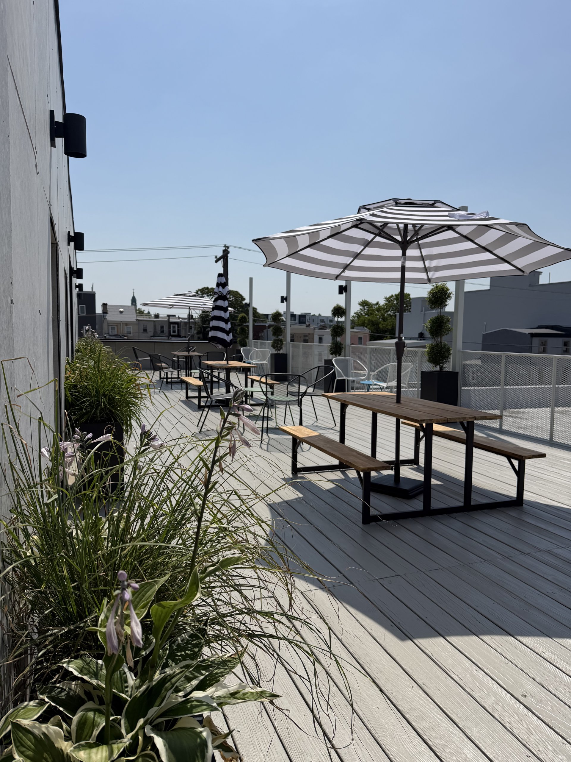 The roofdeck at Billy Penn Studios, with tables, chairs, striped umbrellas and planters